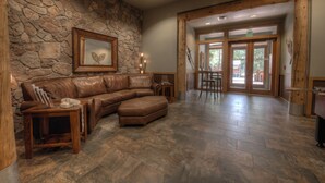A spacious living area with a stone wall, a leather sectional sofa, and a wooden coffee table. - Walk to Lifts! Free Covered Parking, High Ceilings (Dillon)