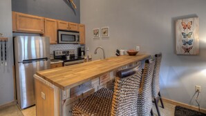 A kitchen with wooden cabinets, stainless steel appliances, a wooden countertop, and a woven chair. - Walk to Lifts! Free Covered Parking, High Ceilings (Dillon)