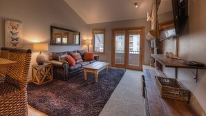 A cozy living room with a leather sofa, a wooden coffee table, and a large mirror. There is a stone fireplace and a wooden bench. - Walk to Lifts! Free Covered Parking, High Ceilings (Dillon)