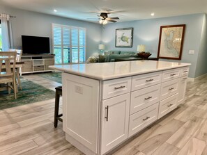 A spacious kitchen with a large island, white cabinetry, and a ceiling fan.