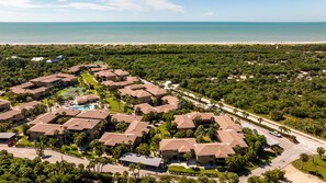 A residential area with multiple houses, a swimming pool, and a beach in the background.