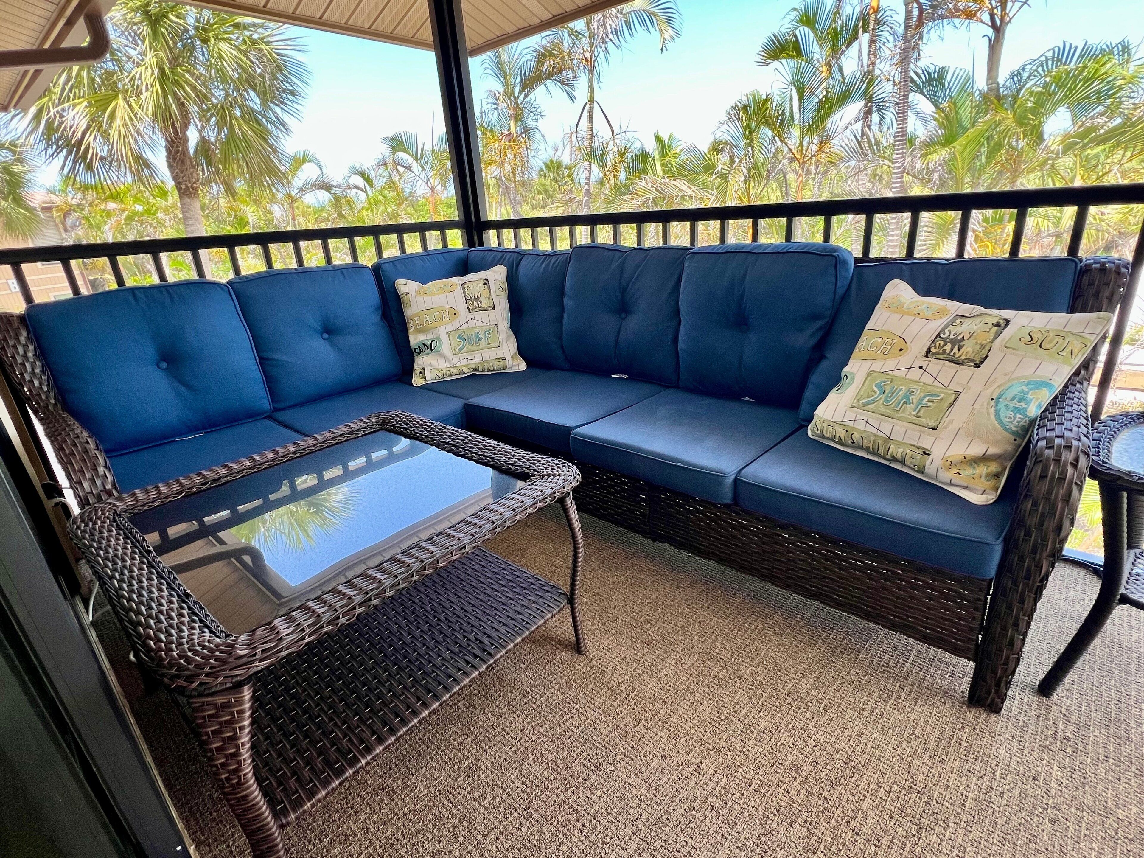 A blue sofa with beach-themed cushions, a glass-top coffee table, and a wicker chair.