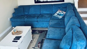 A modern living room with a blue sectional sofa, a white coffee table, and a flat-screen TV mounted on the wall. - Just steps from the Beach and Boardwalk! Perfect vacation getaway! (North Wildwood)