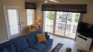A living room with a blue sofa, a coffee table, a television, and a sliding glass door leading to an outdoor area. - Just steps from the Beach and Boardwalk! Perfect vacation getaway! (North Wildwood)