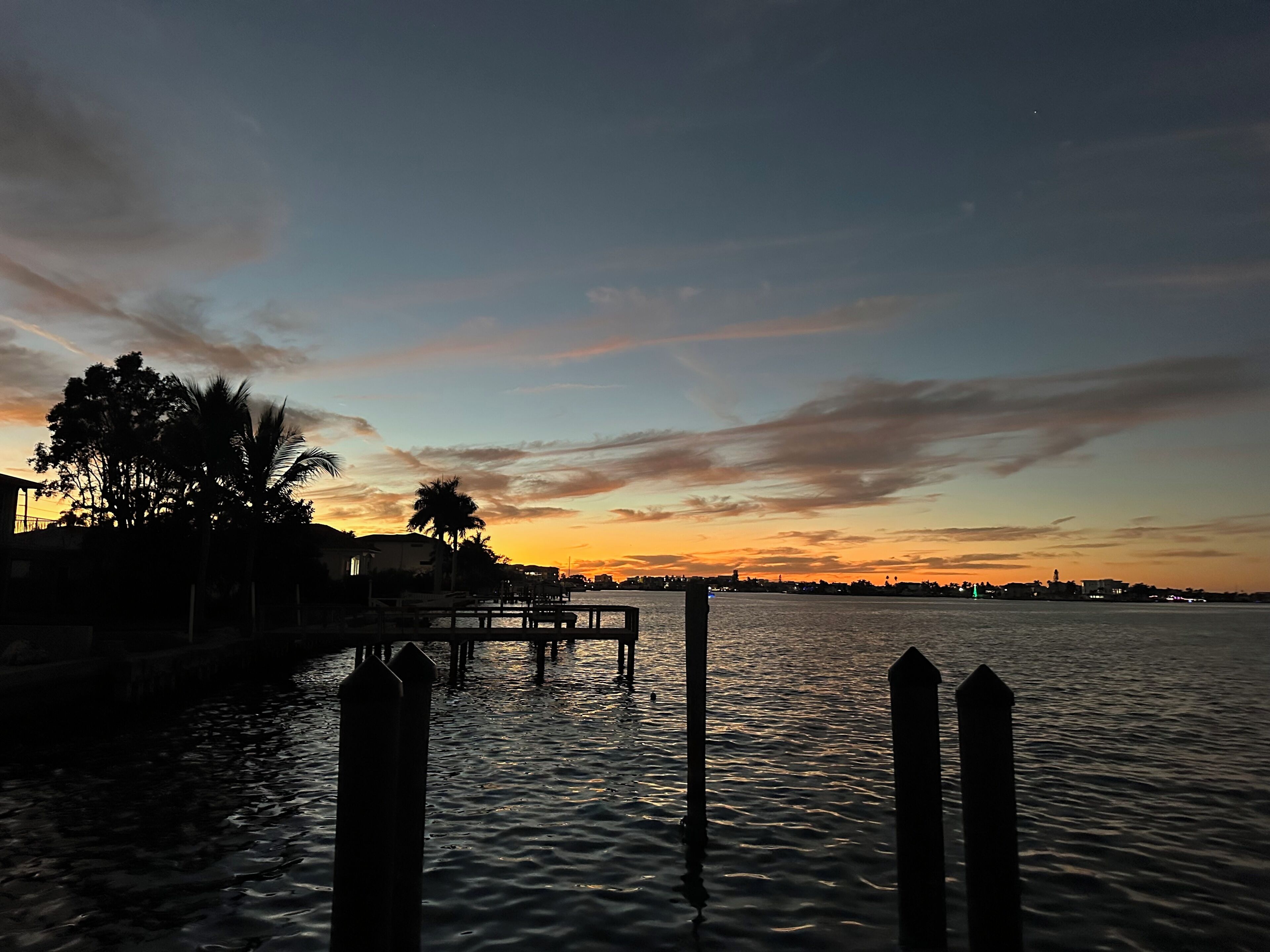A waterfront view with a dock and trees at sunset.