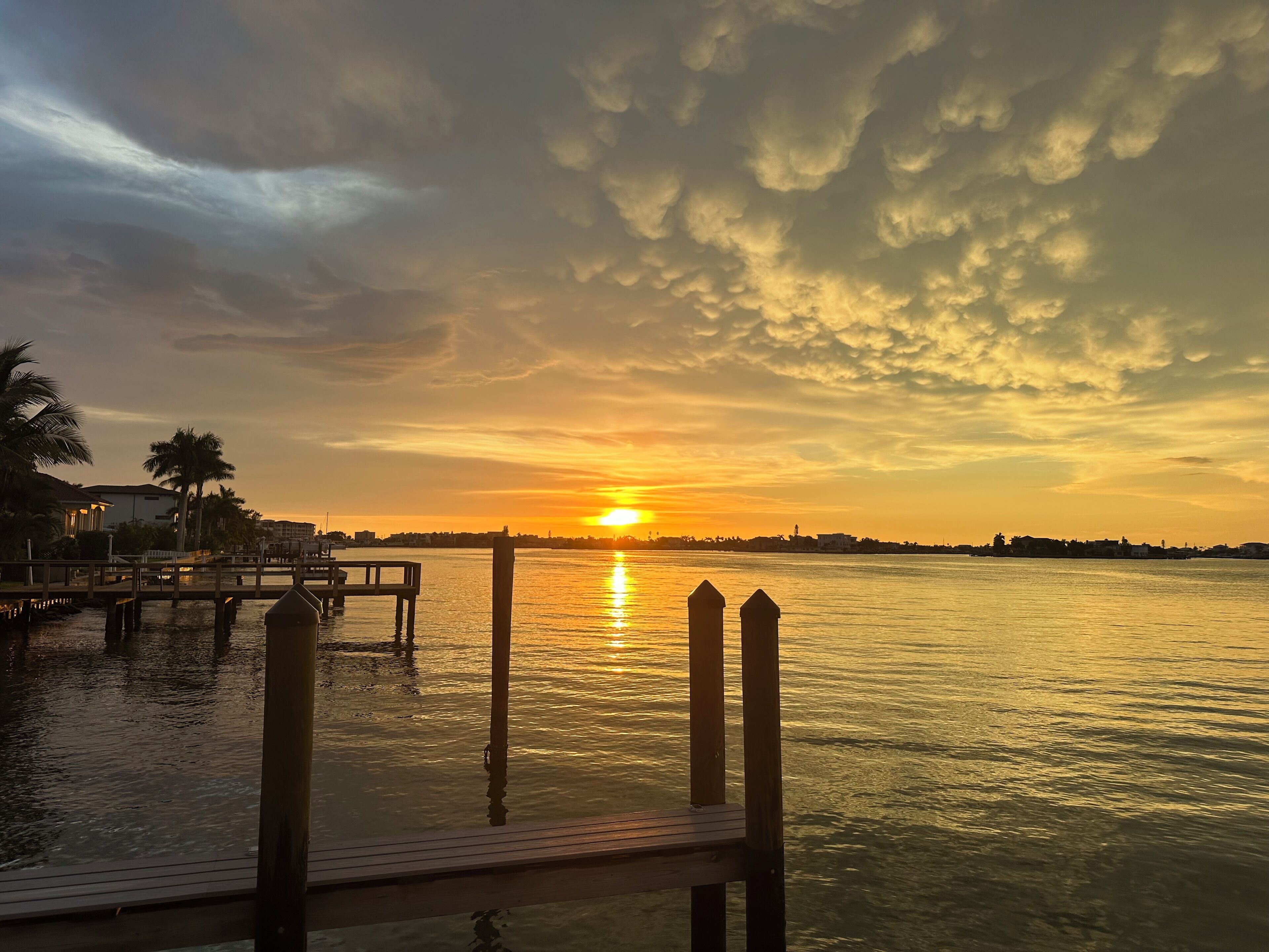 A sunset over a calm body of water with a dock and a distant shoreline.