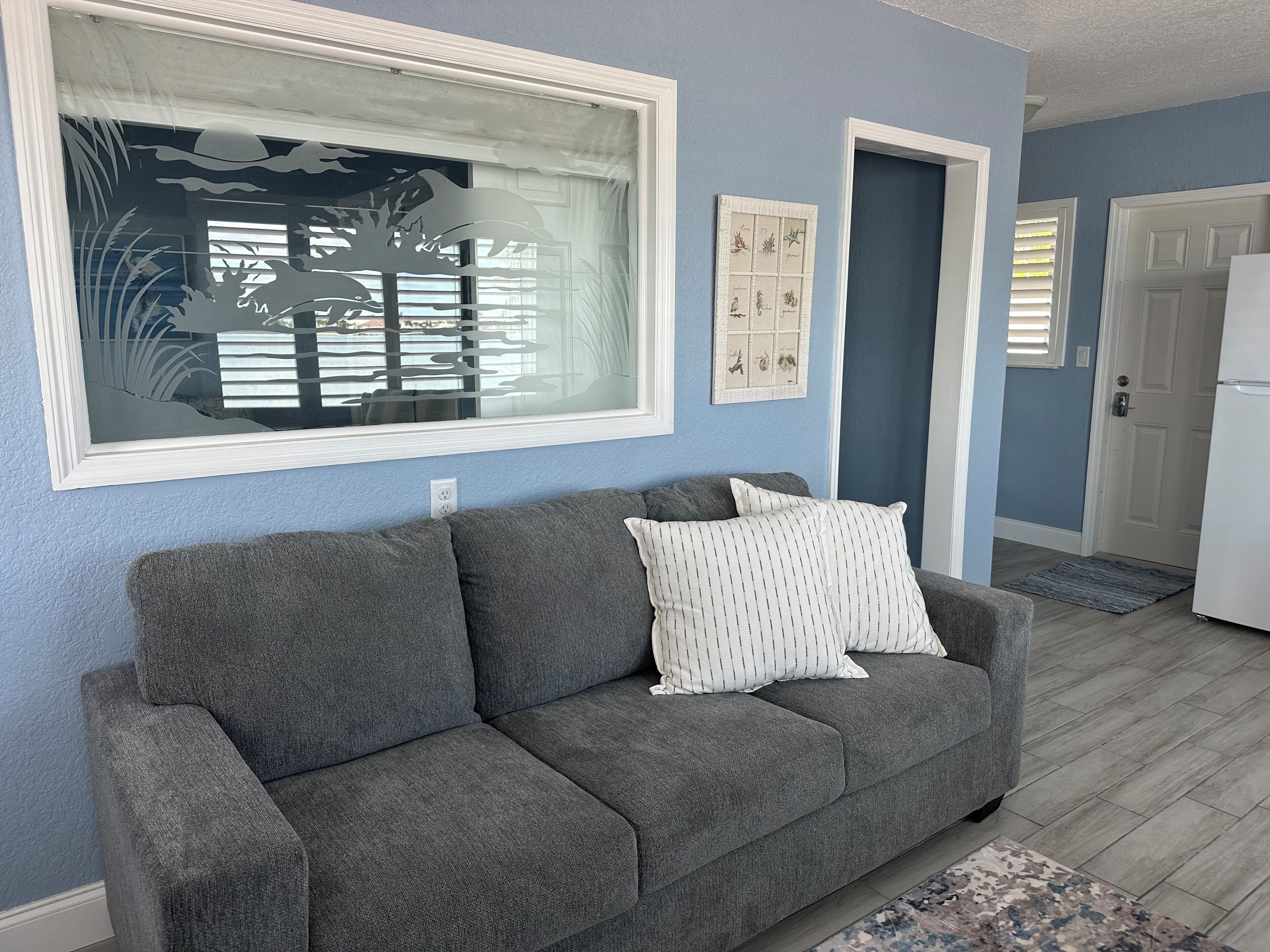 A grey sofa with striped pillows, a window with a tree silhouette, and a door in a room with blue walls.