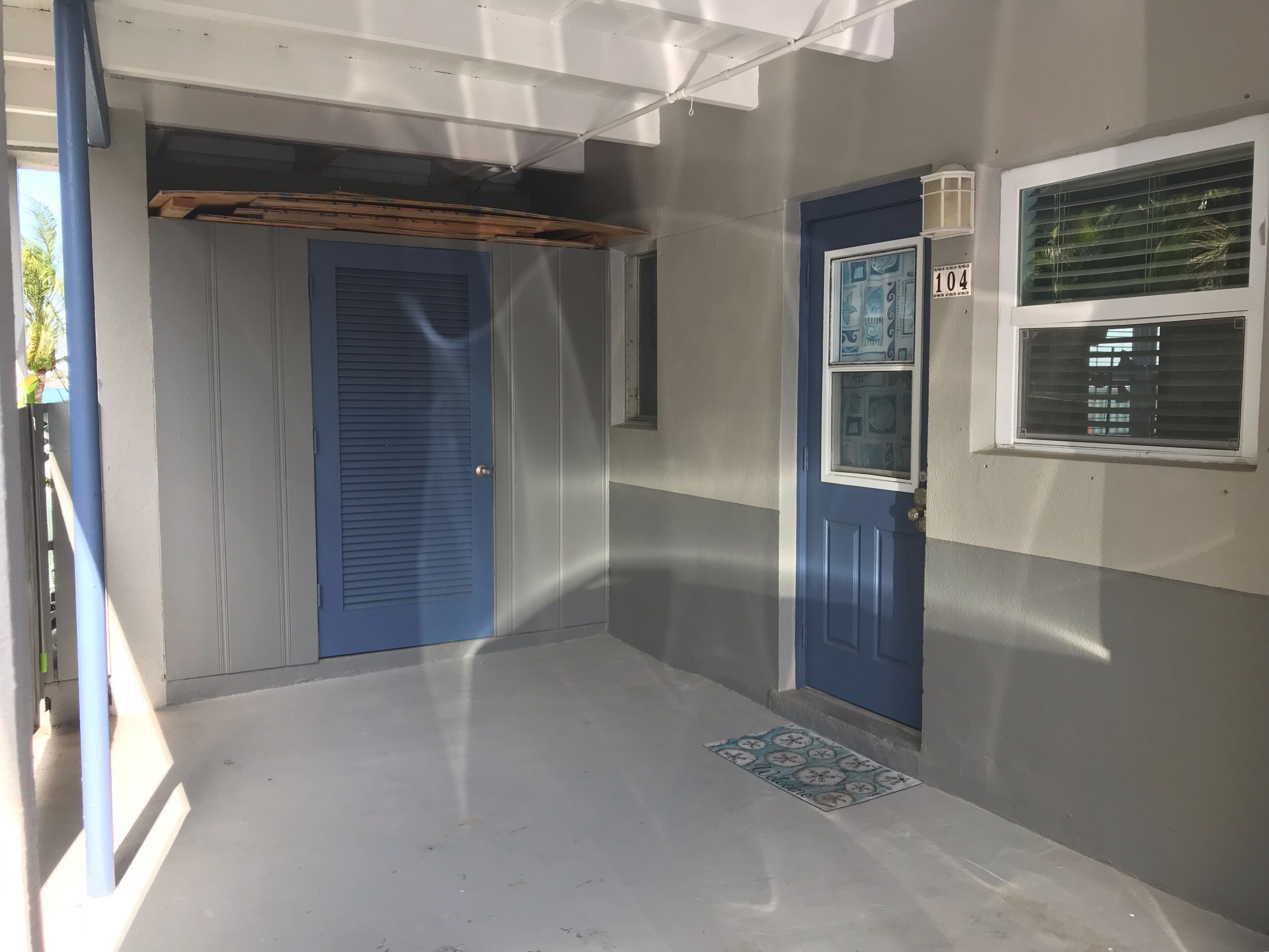 Un couloir avec une porte bleue, une fenêtre avec des stores et un paillasson.