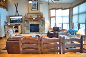 A cozy living room with a stone fireplace, leather furniture, and a television displaying 'Unlimited Plans'.