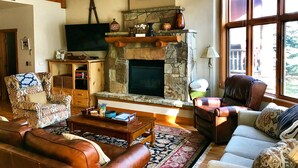 Un salon chaleureux avec une cheminée en pierre, des meubles en cuir et une grande fenêtre offrant une belle vue.