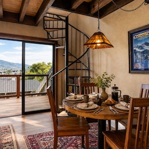 A dining area with a wooden table set for four, a staircase, and a view of a mountainous landscape.