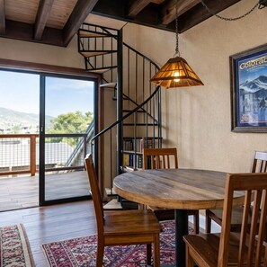 Step into your cozy mountain retreat, where exposed wooden beams and warm pendant lighting welcome you. A spiral staircase invites you upward while your dining space opens to a sunny balcony showcasing peaceful hillside views. - Quitting Time Ultimate Old Town Adventure Basecamp 447 (Park City)