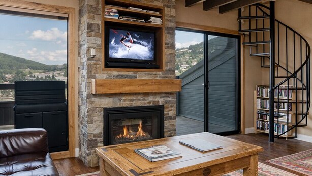 A living room with a stone fireplace, a television mounted on the wall, a leather sofa, a wooden coffee table, and a spiral staircase.