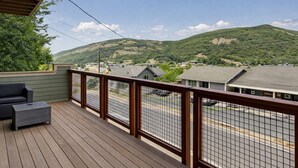 A wooden deck with a metal railing overlooking a residential area and hills.