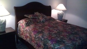 Una cama con una colcha estampada con flores, dos lámparas de noche y una mesita de noche con lámpara.
