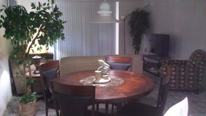 Un comedor con una mesa redonda de madera, sillas, un centro decorativo y una planta en maceta.