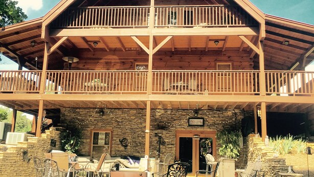Una cabaña de madera de dos pisos con balcón, paredes de piedra y mobiliario exterior.