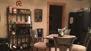 Un comedor con una mesa de madera y cuatro sillas, una estantería, un refrigerador y una puerta.