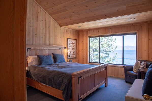 Camera da letto in una baita di legno, con un letto, una finestra vista sull'acqua e un piccolo angolo salotto.