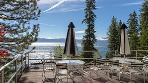 A deck with outdoor seating, overlooking a body of water and mountains.
