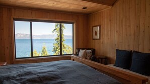 A bedroom with a large window, wooden walls, a bed, and a bench with pillows.