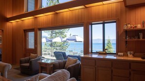 A cozy room with wooden paneling, a large window overlooking a pool area, and a kitchen counter with various items.