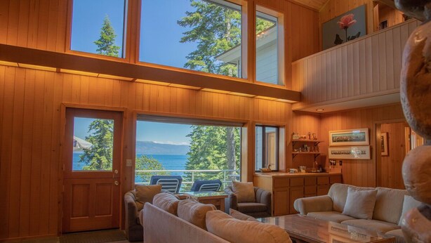 A spacious living room with a large window overlooking a scenic view, a cozy seating area, and a wooden interior.