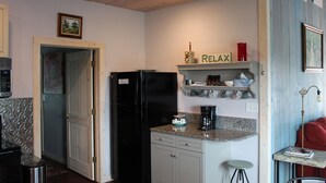 Una cocina compacta con refrigerador, cafetera y un taburete pequeño.