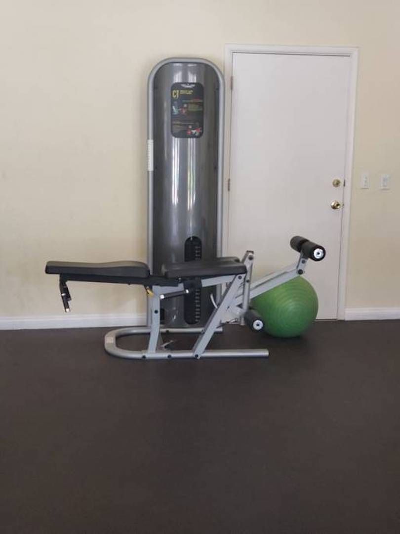 Ein Fitnessraum mit einer Langhantelbank, einem Brustpressgerät und einem grünen Medizinball.
