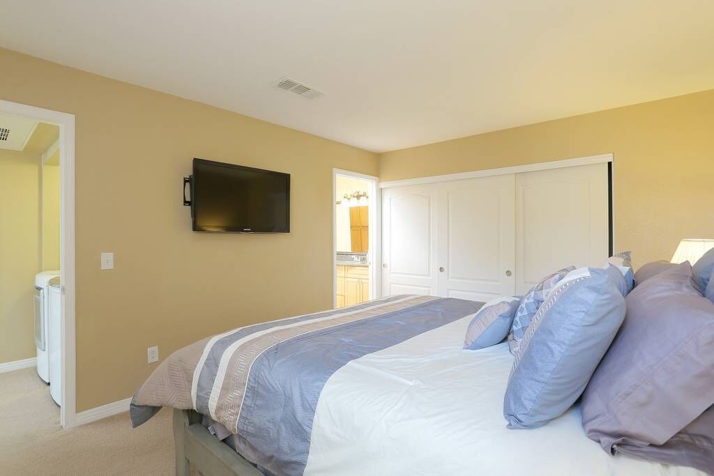 A bedroom with a bed, a television mounted on the wall, and a door leading to a bathroom.