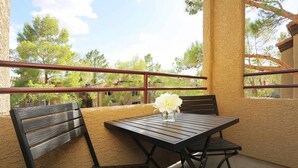 Un balcon avec une table et des chaises en bois, un vase avec une fleur et une vue sur les arbres et les bâtiments.