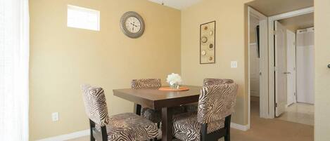 A dining room with a wooden table and zebra-patterned chairs, a wall clock, and a ceiling fan.