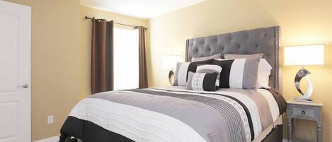 A bedroom with a large bed, a bedside table with a lamp, and a door.