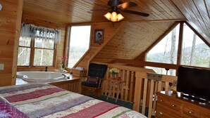 Un chalet confortable avec un grand lit, un ventilateur de plafond, une télévision et une baignoire.