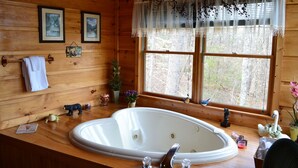 L’intérieur d’un chalet en bois, avec une grande baignoire, des murs en bois, des tableaux encadrés et une fenêtre donnant sur la forêt.