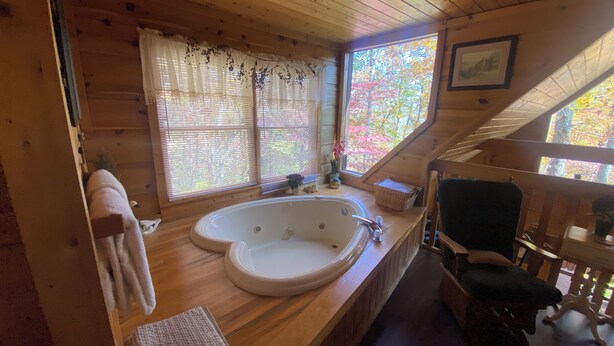 L’intérieur d’une cabane est aménagé avec du bois, il y a une grande baignoire, une fenêtre donnant sur la forêt et un fauteuil.