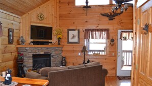L’intérieur d’un chalet confortable, avec une cheminée, des murs en bois, un canapé et un téléviseur.