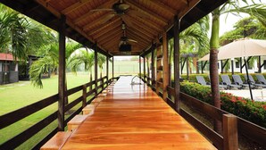 Un espace extérieur abrité, aménagé avec une longue table en bois, des bancs et offrant une vue sur un court de tennis.