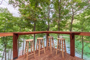 Un ponte in legno con tre sgabelli di legno, affacciato su uno specchio d'acqua sullo sfondo di alberi.