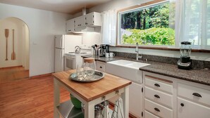A modern kitchen with white cabinets, a granite countertop, a built-in stove, and a window with a view of greenery. - Relaxing Retreat in the Redwoods, Spa, Dog Friendly! (Cazadero)