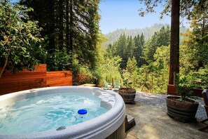 Ein Whirlpool, umgeben von einer Holzterrasse, mit Blick auf einen bewaldeten Hügel.