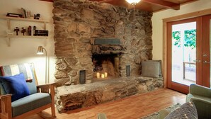 A stone fireplace with a ceiling fan, wooden floors, and a view through a glass door. - Relaxing Retreat in the Redwoods, Spa, Dog Friendly! (Cazadero)