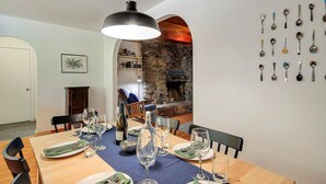 A dining area with a wooden table set for a meal, a stone fireplace, and a wall with various spoons. - Relaxing Retreat in the Redwoods, Spa, Dog Friendly! (Cazadero)