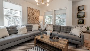 Un salon moderne avec un canapé d’angle gris, une table basse en bois et un élément décoratif mural.