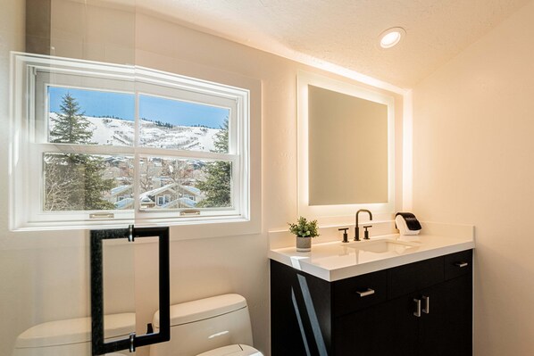 Une salle de bain avec une fenêtre, un lavabo, un miroir et des toilettes.
