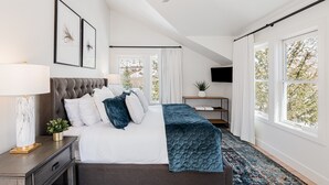 Une chambre à coucher comprenant un lit, une table de chevet, une lampe, des tableaux encadrés, un téléviseur et de grandes fenêtres.