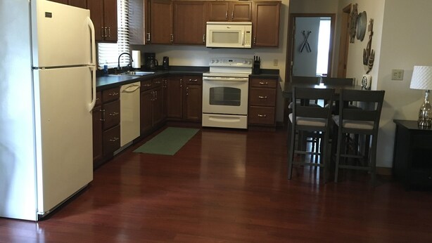 Una cocina con armarios de madera, un refrigerador, un microondas, un horno y un comedor con sillas y una mesa.