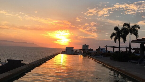 Ein langer, schmaler Pool mit Sonnenuntergang im Hintergrund.