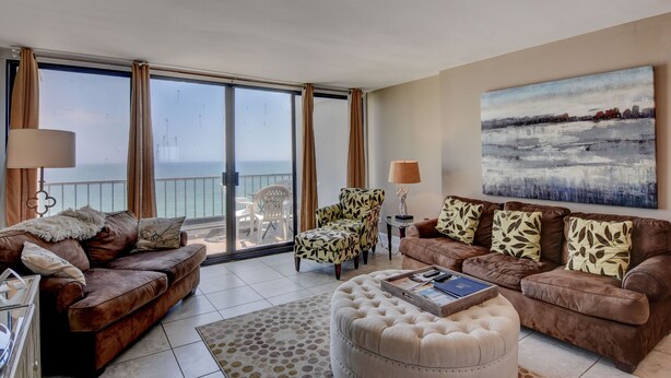 A spacious living room with a balcony, leather sofas, a patterned armchair, and a large painting. - Station One - 8I From - Oceanfront condo with community pool, tennis, beach (Wrightsville Beach)
