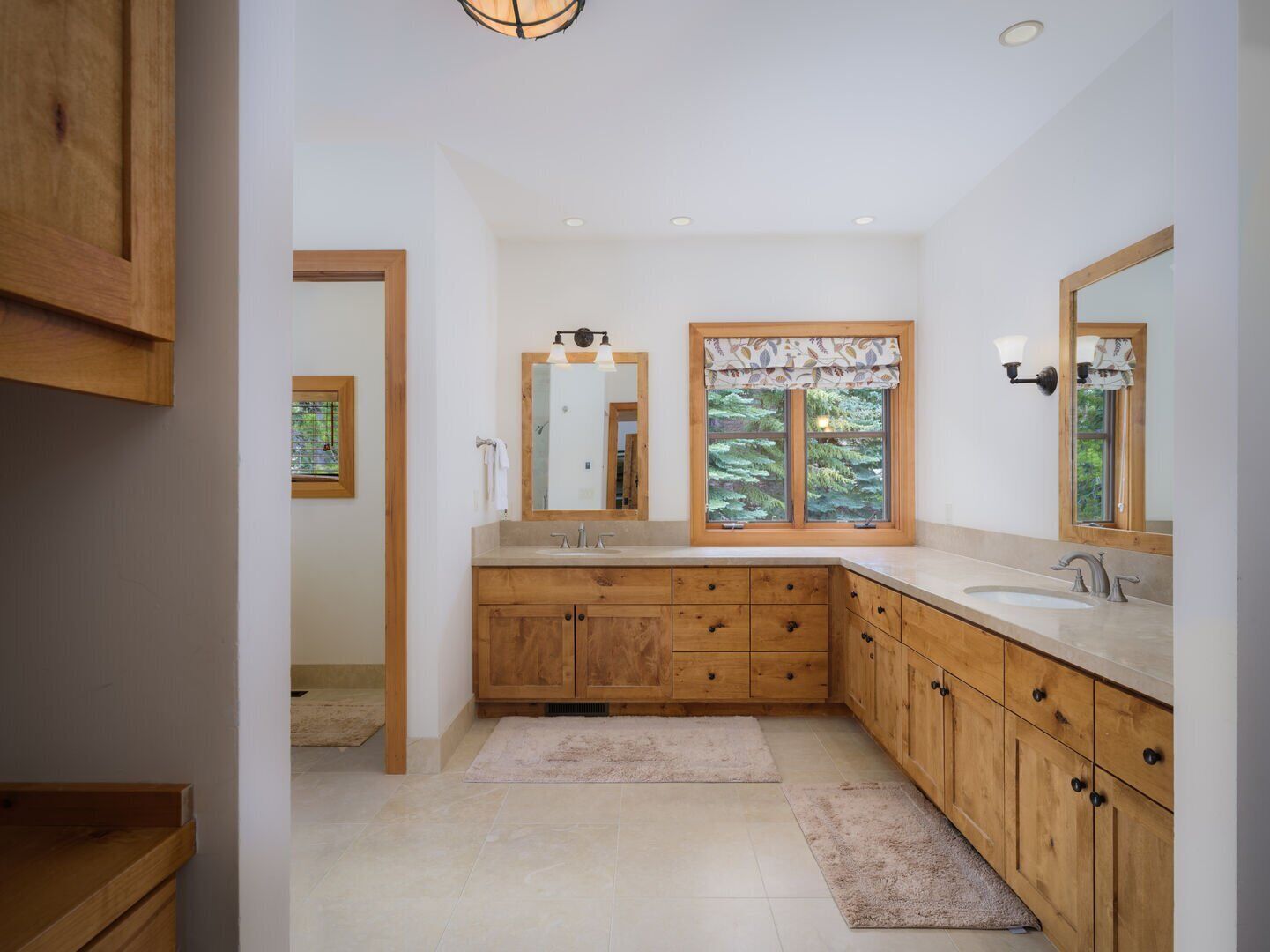 Une salle de bain moderne avec des meubles en bois, un grand miroir, une fenêtre donnant sur les arbres et un luminaire.